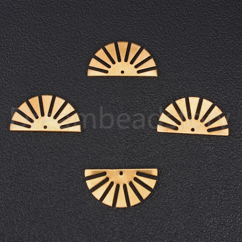 May include: Four gold-colored metal sunburst shapes, each with a hole in the center. The sunbursts are arranged in a diamond pattern on a black background.