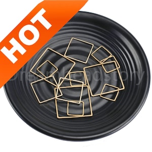 May include: A collection of gold-toned metal square jump rings on a black plate. The jump rings are various sizes and are perfect for jewelry making.
