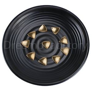 May include: A collection of ten gold-colored triangle-shaped metal embellishments on a black plate.