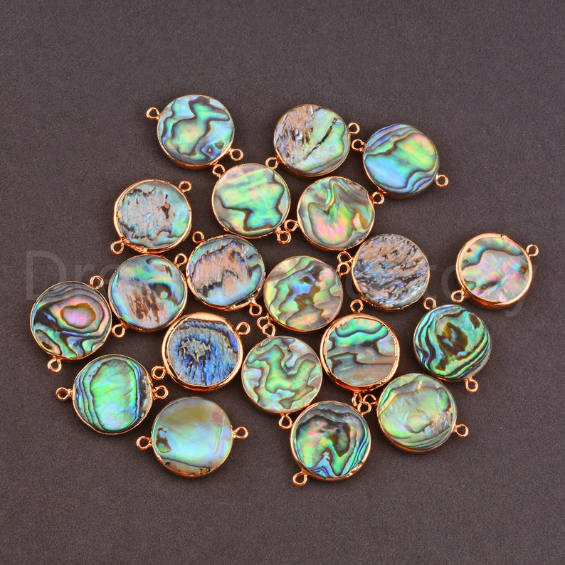 May include: A collection of 18 round abalone shell connector charms with gold-toned metal accents. The charms have a variety of iridescent colors, including green, blue, and purple.