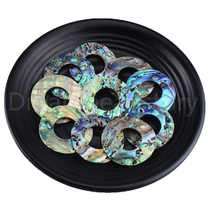 May include: A collection of iridescent abalone shell rings, each with a unique pattern of blue, green, and gold hues. The rings are arranged in a black bowl.
