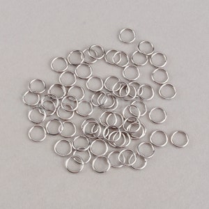 May include: A large quantity of silver jump rings, a type of metal ring used in jewelry making.