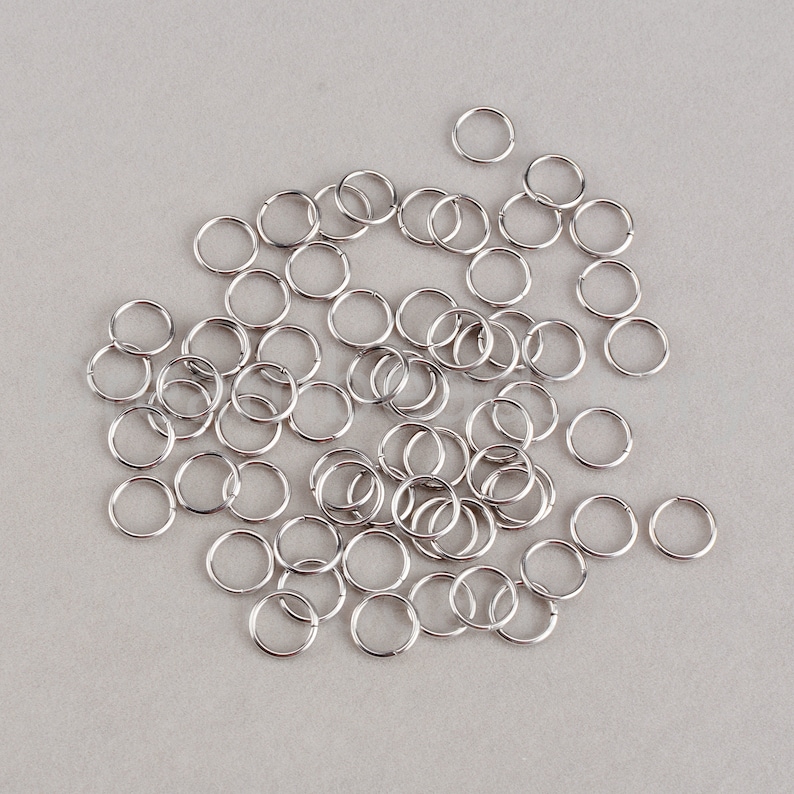 May include: A large quantity of silver jump rings, a type of metal ring used in jewelry making.