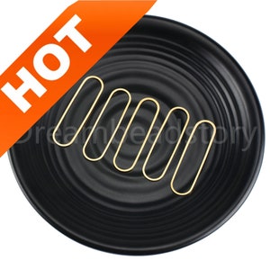 May include: Five gold oval-shaped jump rings on a black background. The jump rings are arranged in a row, with the largest ring at the top and the smallest ring at the bottom.