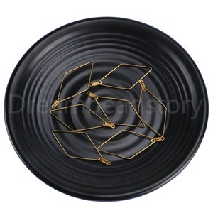 May include: A group of eight gold-colored diamond-shaped wire loops with a small loop at each end. The loops are arranged in a random pattern on a black surface.