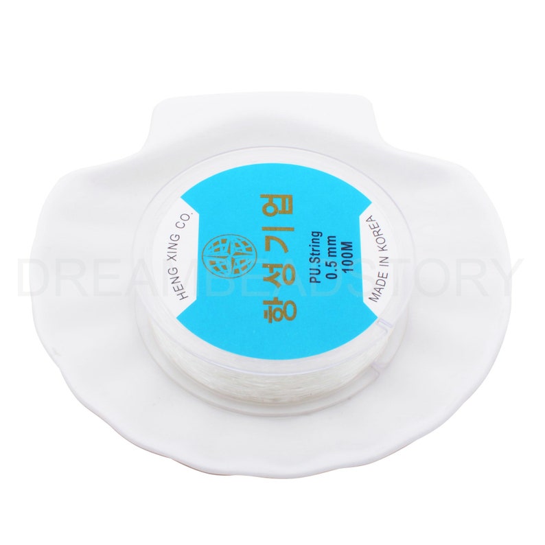 Puede incluir: Una bobina blanca de cuerda de PU de 0,5 mm, etiquetada "항성기업" en coreano, con un fondo azul y el texto "PU String 0.5 mm 100M" en ingl&eacute;s. La bobina est&aacute; en un plato de cer&aacute;mica blanco.