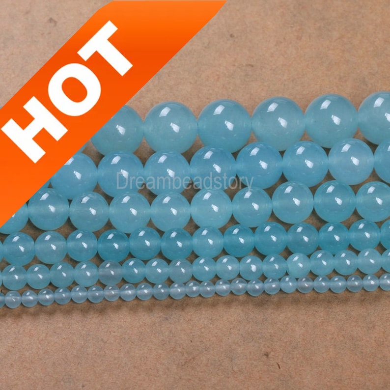 May include: Assortment of light blue round gemstone beads in various sizes. The beads are arranged in rows, with the largest beads at the top and the smallest beads at the bottom. The beads are smooth and polished, and they have a translucent appearance.