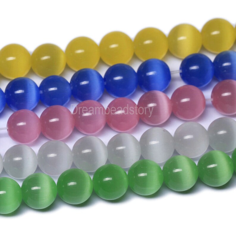 May include: A strand of round, iridescent glass beads in various colors, including yellow, blue, pink, white, and green. The beads have a cat's eye effect, with a line of color running through the center of each bead.