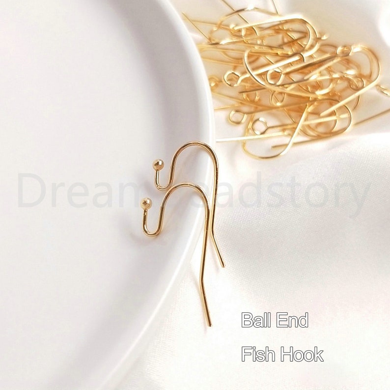May include: Two gold ball end fish hook earring findings. The hooks are made of metal and have a smooth, shiny finish.