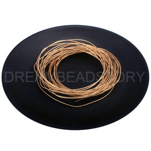 Pode incluir: Uma bobina de fio dourado em um prato preto. O fio tem aproximadamente 1 mm de espessura.