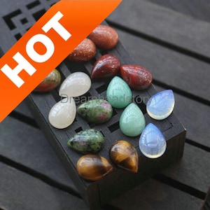 May include: Assortment of teardrop-shaped gemstones in various colors, including red, green, white, and brown. The gemstones are displayed on a dark wooden surface. The word "HOT" is displayed in white text on an orange banner.