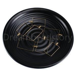 May include: A set of eight gold-toned metal earring blanks in a square shape. The blanks are displayed on a black plate.