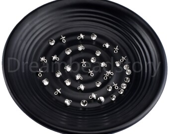 May include: A collection of small, silver-colored metal bead caps, each with a rounded cap and a loop, scattered on a black, ridged plate. The caps are evenly distributed, creating a pattern. The image is well-lit, highlighting the metallic sheen.
