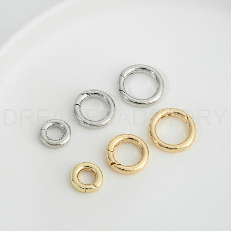 Op de afbeelding: Assortiment van zilveren en gouden metalen springringen. De springringen zijn in verschillende maten en zijn gerangschikt op een wit oppervlak.
