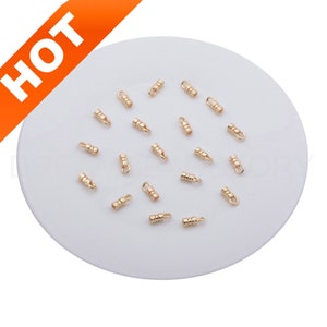 May include: A close-up of a group of 20 gold-colored metal crimp end caps. The caps are arranged on a white surface.