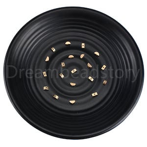 May include: A collection of gold-colored metal beads in various shapes, including half-circles and squares, displayed on a black plate.