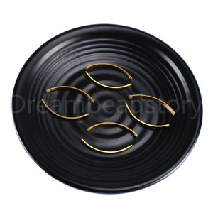 May include: A set of six gold-colored metal jewelry findings in the shape of an arch. The findings are arranged on a black plate.