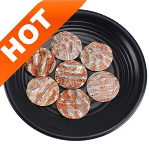 Può includere: Sette pezzi rotondi, bianchi e arancioni, iridescenti, simili a conchiglie, decorativi su un piatto nero.