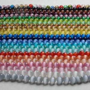 May include: A collection of round, iridescent glass beads in various colors, including purple, green, yellow, blue, turquoise, red, pink, white, and gray. The beads are arranged in rows, creating a colorful and eye-catching display.