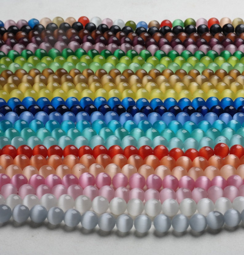 May include: A collection of round, iridescent glass beads in various colors, including purple, green, yellow, blue, turquoise, red, pink, white, and gray. The beads are arranged in rows, creating a colorful and eye-catching display.