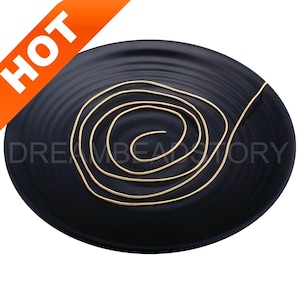 May include: A gold snake chain necklace on a black plate. The chain is coiled in a spiral shape.