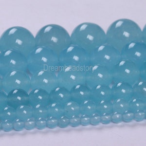 May include: A collection of round, light blue gemstone beads of varying sizes. The beads are smooth and polished, with a translucent appearance.