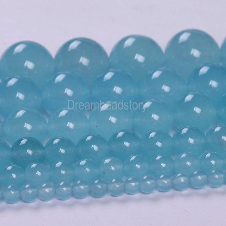 May include: A collection of round, light blue gemstone beads of varying sizes. The beads are smooth and polished, with a translucent appearance.