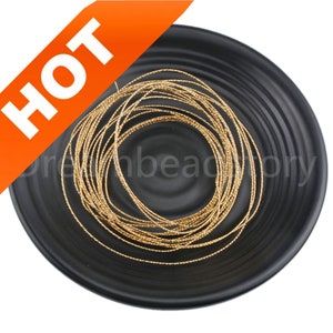 May include: A close-up of a spool of gold metallic cord on a black plate. The cord is thin and has a shiny finish.