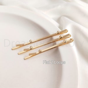 May include: Three gold hair clips with two loops on each clip. The clips are flat and have a smooth finish. The text "Flat 2 Loops" is visible below the clips.