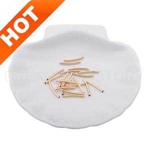 May include: A pile of gold-colored metal tube beads on a white ceramic shell-shaped dish.