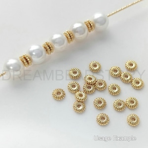May include: Gold-coloured metal bead spacers with a flower-like design. The spacers are shown next to a strand of white pearls with gold-coloured metal bead spacers.