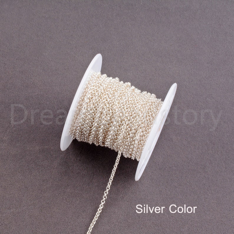 Peut inclure: Une bobine de cha&icirc;ne de couleur argent&eacute;e, enroul&eacute;e autour d'une bobine en plastique blanc. La cha&icirc;ne est de style d&eacute;licat &agrave; maillons fins.