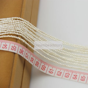 May include: A close-up of a white pearl strand, measuring 65 inches long, with a white measuring tape.