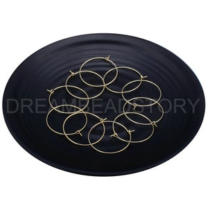 May include: A set of eight gold-toned hoop earrings on a black plate. The hoops are arranged in a circular pattern.