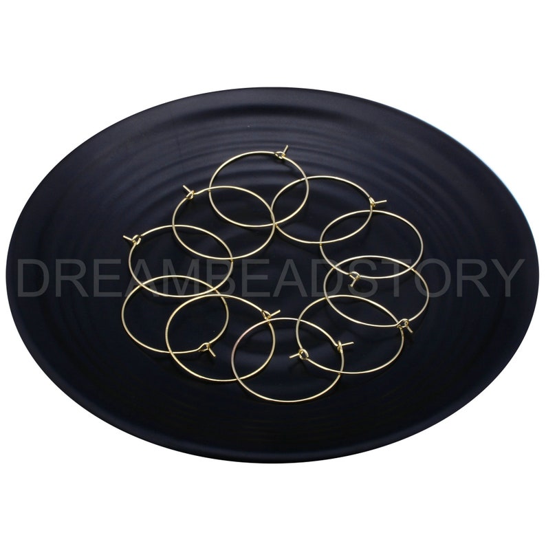 May include: A set of eight gold-toned hoop earrings on a black plate. The hoops are arranged in a circular pattern.