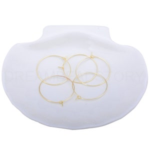 May include: Four gold-coloured hoop earrings with a small opening on each hoop. The earrings are arranged in a circle on a white surface.