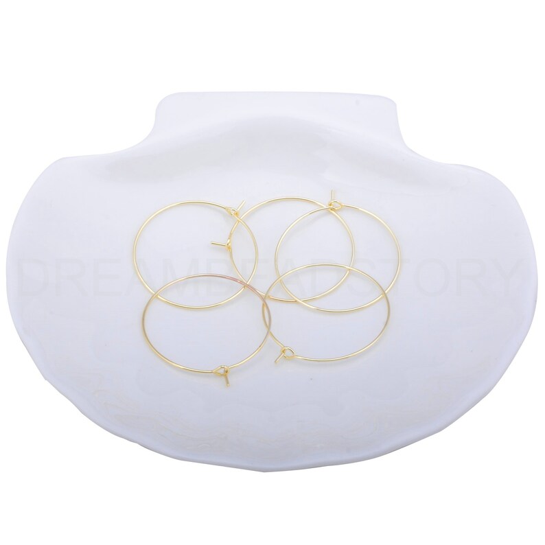 May include: Four gold-coloured hoop earrings with a small opening on each hoop. The earrings are arranged in a circle on a white surface.