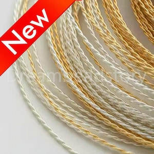 May include: Close-up of a bundle of silver and gold twisted wire. The wire is thin and delicate, and it is arranged in a circular pattern.