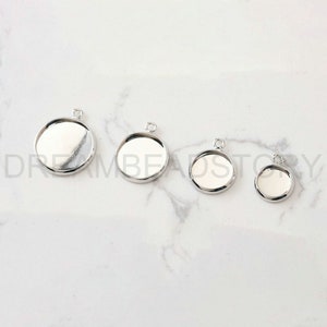 Puede incluir: Cuatro bandejas de colgantes de metal plateadas de diferentes tama&ntilde;os. Las bandejas son redondas y tienen una superficie lisa y reflectante. Son perfectas para crear joyas personalizadas.