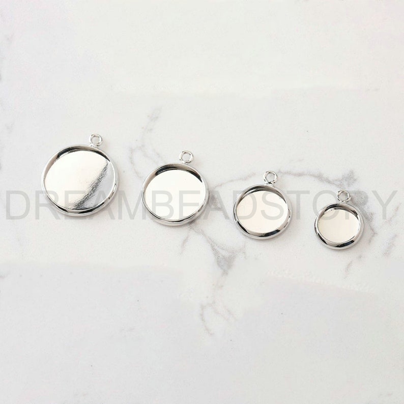 Puede incluir: Cuatro bandejas de colgantes de metal plateadas de diferentes tama&ntilde;os. Las bandejas son redondas y tienen una superficie lisa y reflectante. Son perfectas para crear joyas personalizadas.