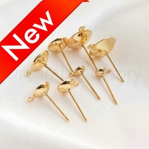 May include: Gold earring findings with a round, flat top and a post. The findings are arranged on a white surface.