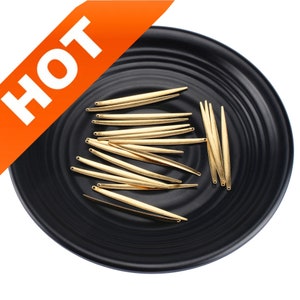 May include: A close-up of a black plate with a collection of gold-colored metal jewelry findings. The findings are long and thin, resembling small, pointed needles.