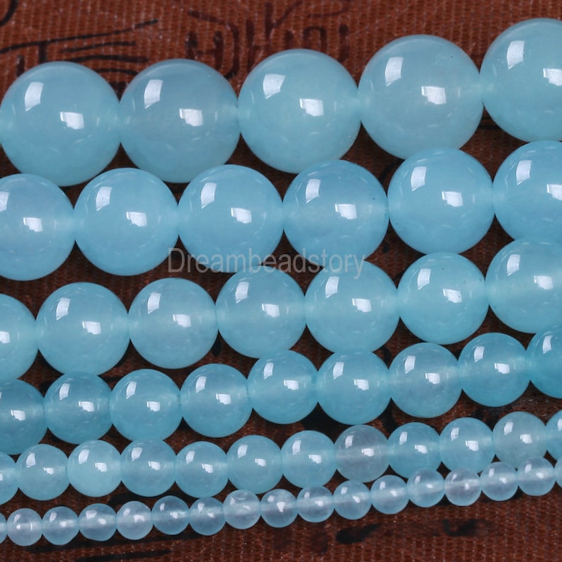 May include: A collection of smooth, round, light blue beads of varying sizes. The beads are made of natural stone and have a polished finish.