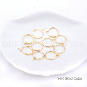 May include: Eight gold-colored hoop earrings on a white plate. 14K Gold Color.
