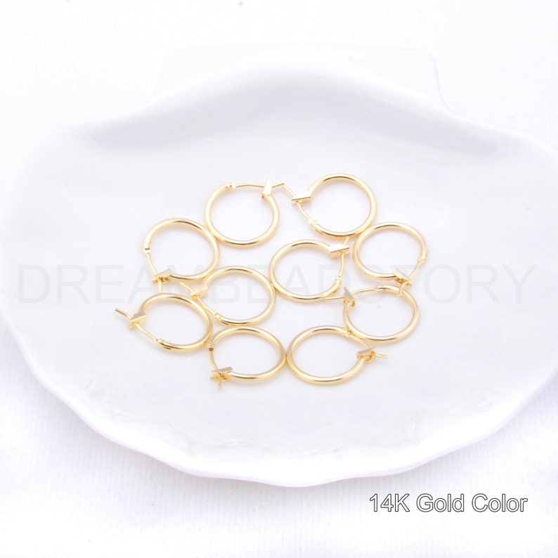 May include: Eight gold-colored hoop earrings on a white plate. 14K Gold Color.