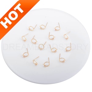 May include: A collection of 12 gold-toned earring posts with a small circle and a single clear rhinestone.
