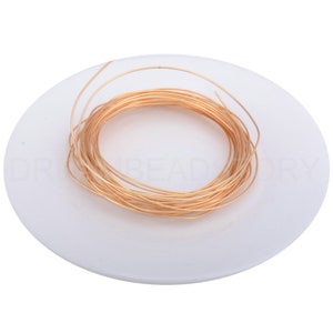 Pode incluir: Uma bobina de fio dourado em uma superf&iacute;cie branca.