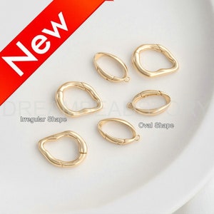 May include: Five gold-toned metal connector charms, two with an irregular shape and three with an oval shape. The charms are on a white surface.