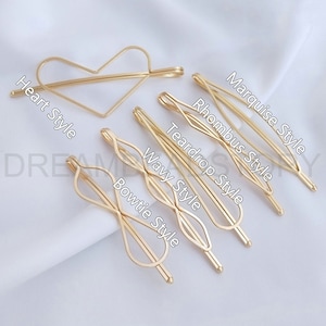 Può includere: Set di sei fermagli per capelli dorati in diverse forme, tra cui stili a forma di cuore, lacrima, rombo, fiocco, ondulato e marquise. I fermagli sono disposti su una superficie bianca.