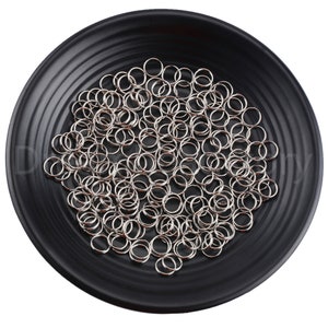 Op de afbeelding: Een zwarte plaat gevuld met zilveren springringen. De springringen zijn klein en rond, en er zijn er veel van.